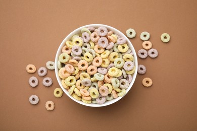 Photo of Tasty cereal rings in bowl on brown table, top view