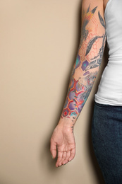 Woman with colorful tattoos on arm against beige background, closeup