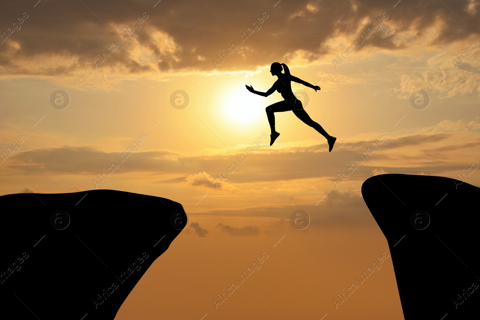 Image of Concept of reaching life and business goals. Silhouette of woman jumping over chasm at sunrise