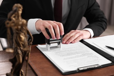 Notary stamping document at wooden table in office, closeup