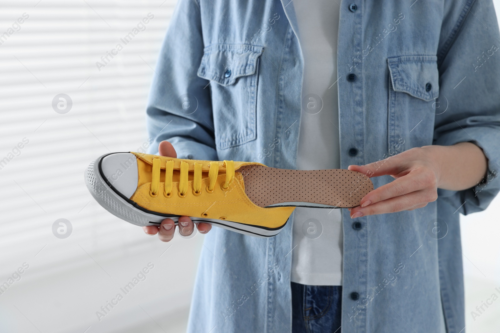 Photo of Woman putting orthopedic insole into shoe indoors, closeup. Foot care