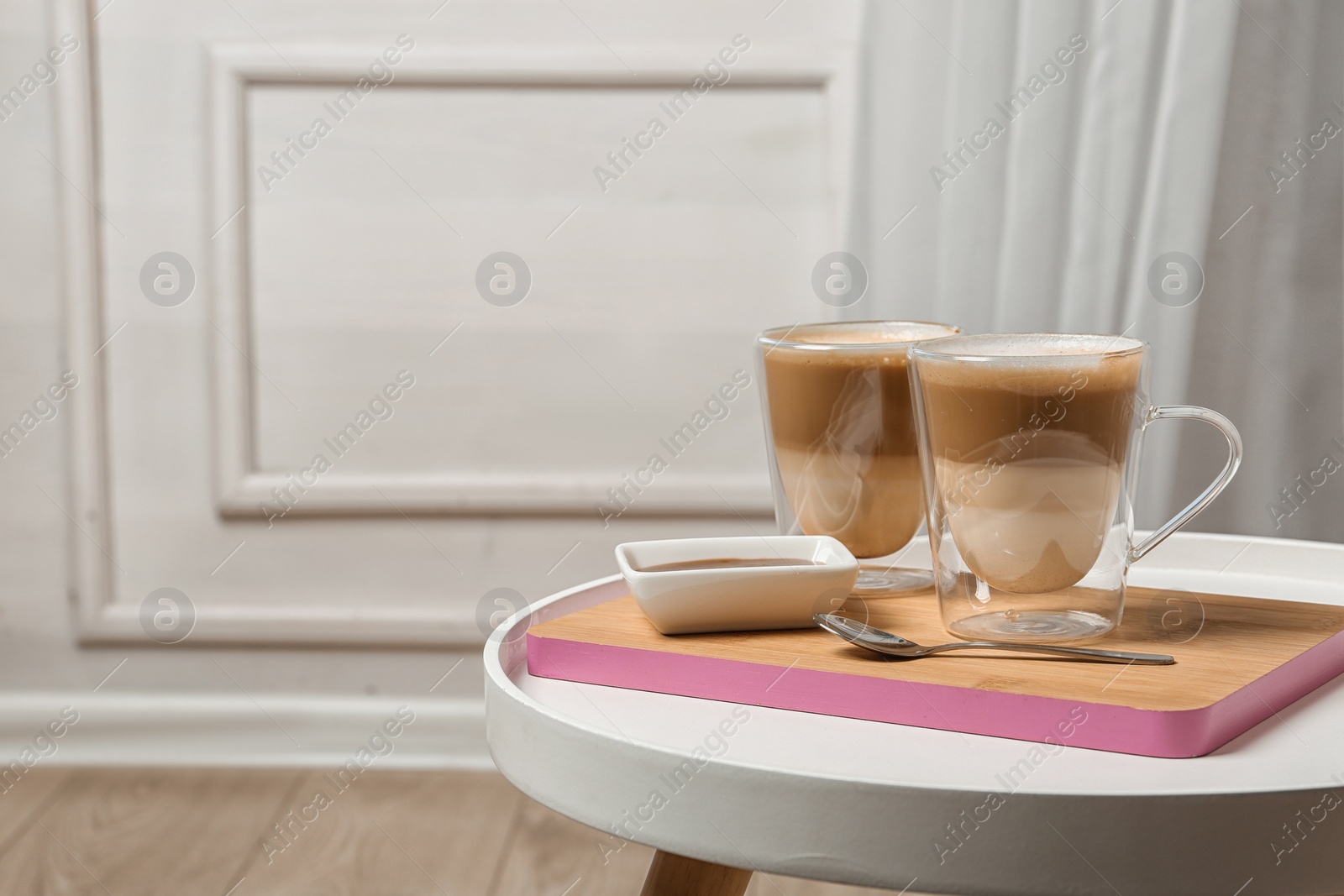 Photo of Glass cups of caramel macchiato and syrup on table, space for text