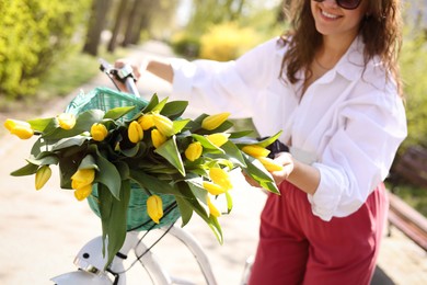 Woman with bicycle and bouquet of yellow tulips outdoors on sunny day, closeup