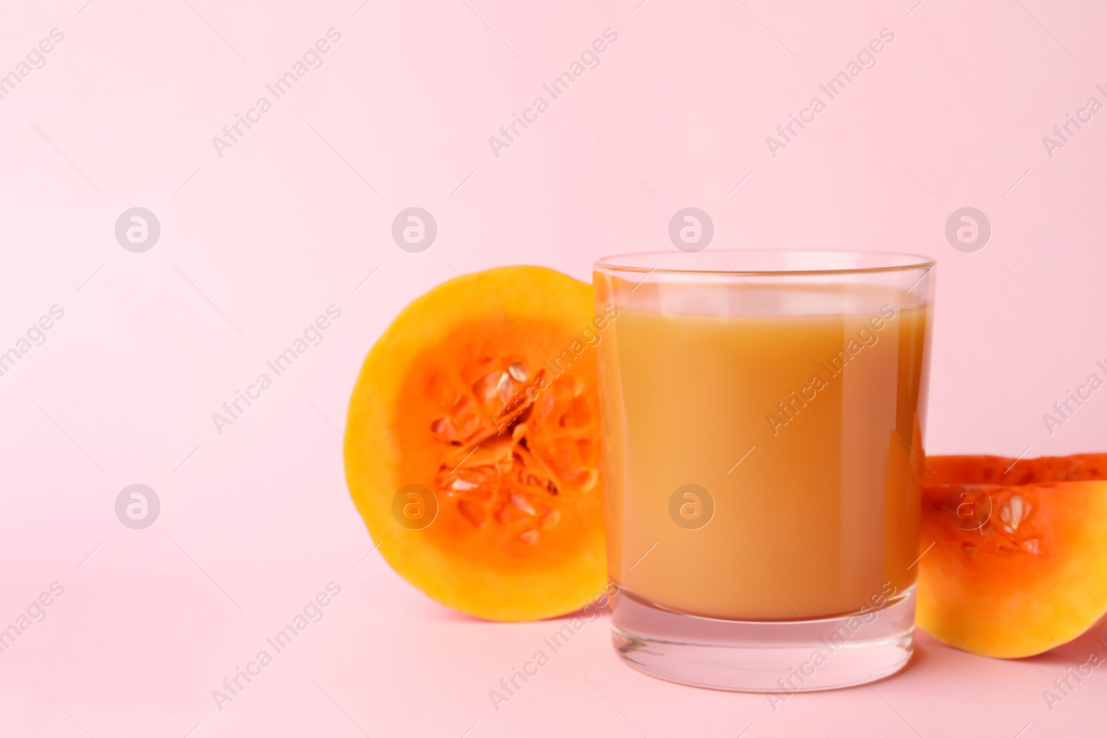 Photo of Tasty pumpkin juice in glass and cut pumpkin on pink background, space for text