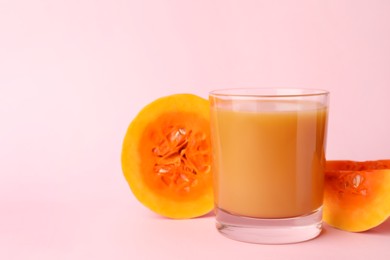Tasty pumpkin juice in glass and cut pumpkin on pink background, space for text