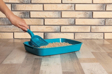 Photo of Woman cleaning cat toilet with scoop on floor. Pet care