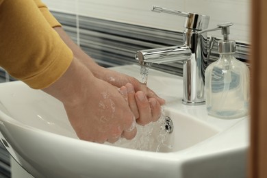 Photo of Man using water tap to rinse soap off hands in bathroom, closeup