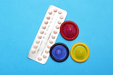 Photo of Condoms and birth control pills on light blue background, flat lay. Safe sex concept