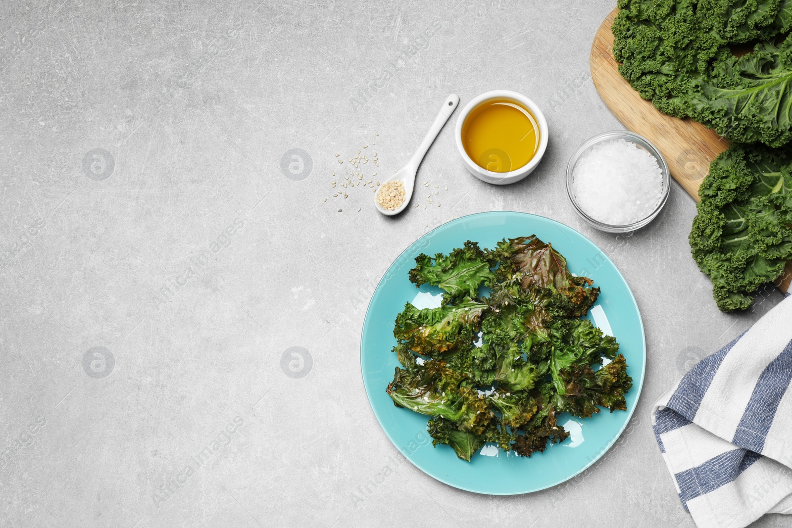 Photo of Tasty baked kale chips on light grey table, flat lay. Space for text