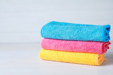 Photo of Stack of colorful microfiber cloths on white table, space for text