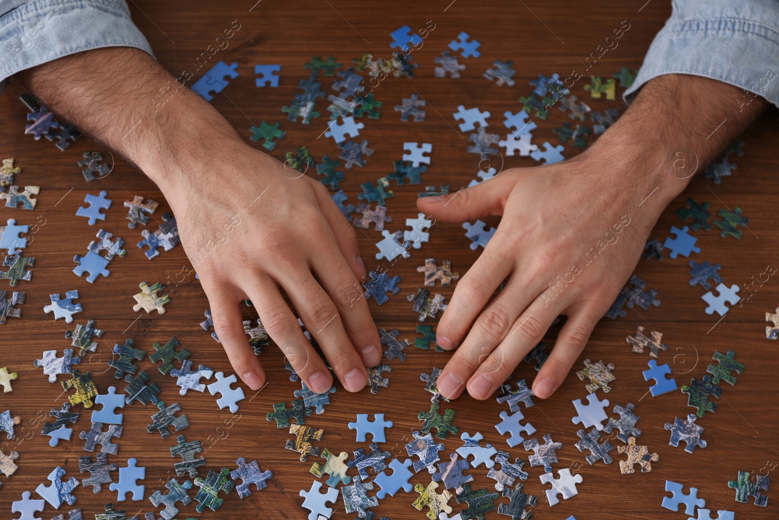 Photo of Man playing with puzzles at wooden table, above view