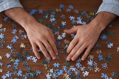 Man playing with puzzles at wooden table, above view