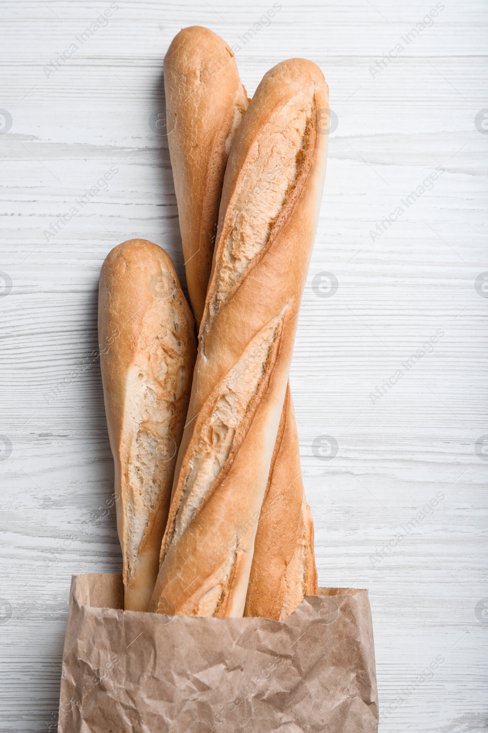 Photo of Tasty baguettes in package on white wooden table, top view