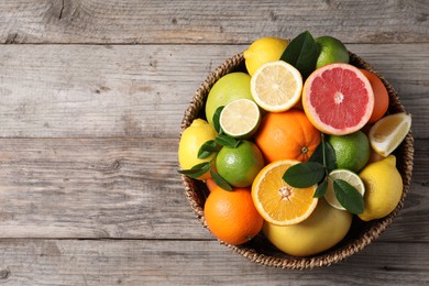 Different fresh citrus fruits and leaves in wicker basket on wooden table, top view. Space for text