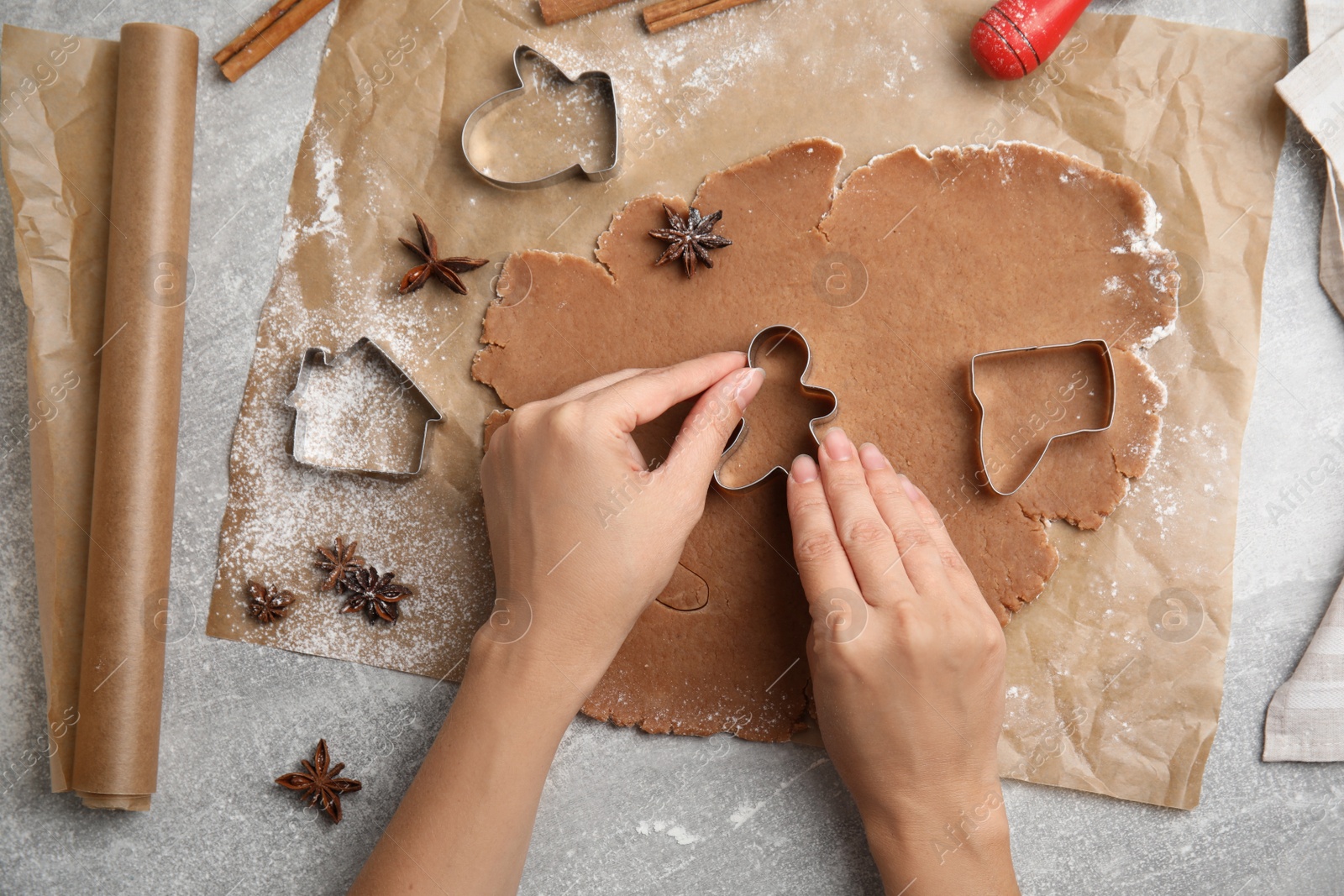 Photo of Woman making Christmas gingerbread cookies at grey table, top view