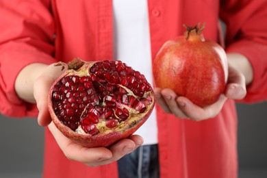 Photo of Woman holding whole and cut pomegranates on grey background, closeup