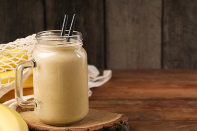 Photo of Mason jar with banana smoothie on wooden table. Space for text