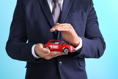 Male insurance agent holding toy car on color background, closeup