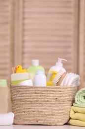 Wicker basket with baby cosmetic products, bath accessories and rubber duck on table indoors