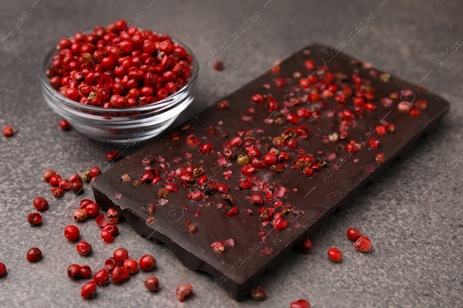 Photo of Delicious chocolate bar and red peppercorns on grey textured table, closeup