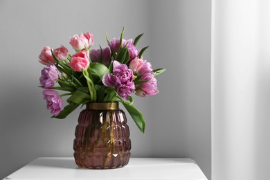 Beautiful bouquet of colorful tulip flowers on white table near light grey wall. Space for text