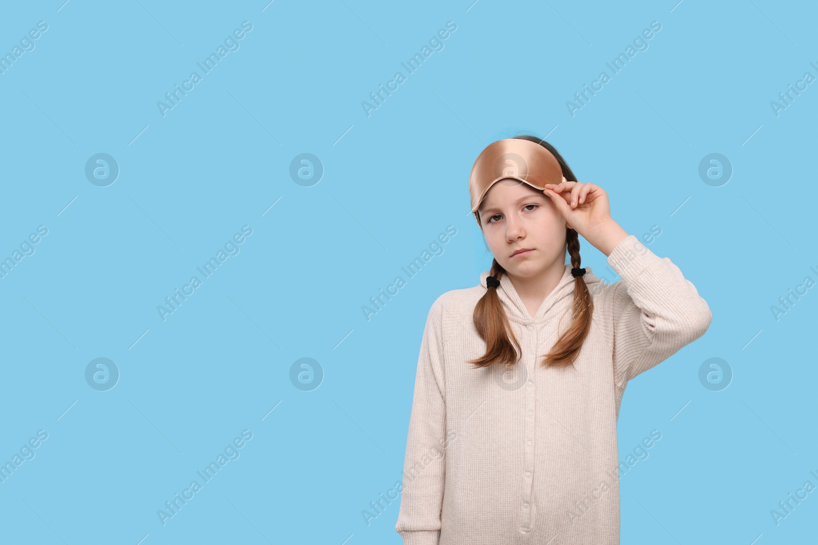 Photo of Girl with sleep mask on light blue background, space for text. Insomnia problem