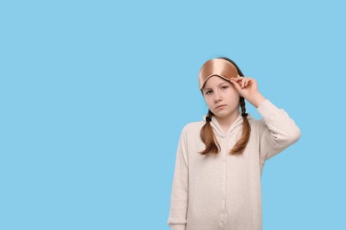 Girl with sleep mask on light blue background, space for text. Insomnia problem