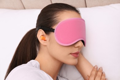 Photo of Young woman with foam ear plugs and mask sleeping in bed, closeup