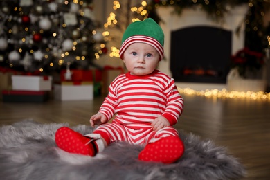 Photo of Cute little baby in Santa's elf clothes on floor at home. Christmas celebration