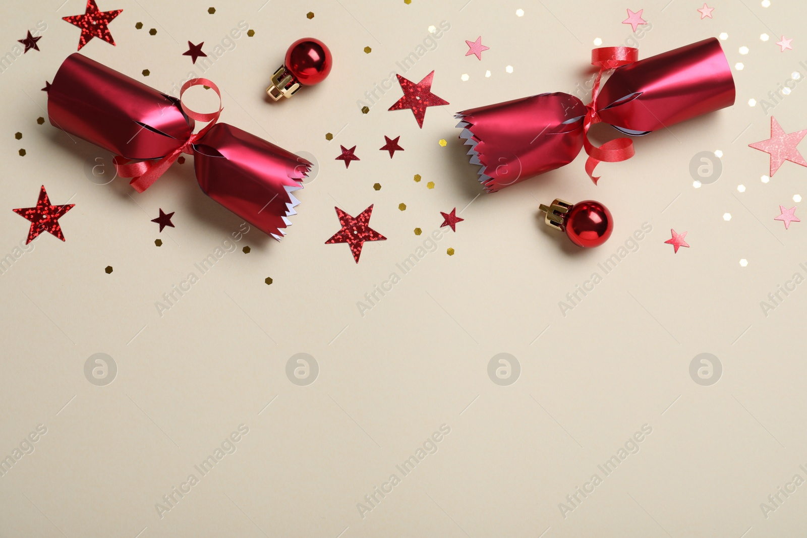 Photo of Open red Christmas cracker and decorations with shiny confetti on beige background, flat lay. Space for text