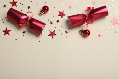 Open red Christmas cracker and decorations with shiny confetti on beige background, flat lay. Space for text