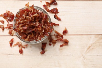 Photo of Pieces of tasty fried bacon in bowl on wooden table, top view. Space for text