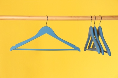 Wooden rack with clothes hangers on color background