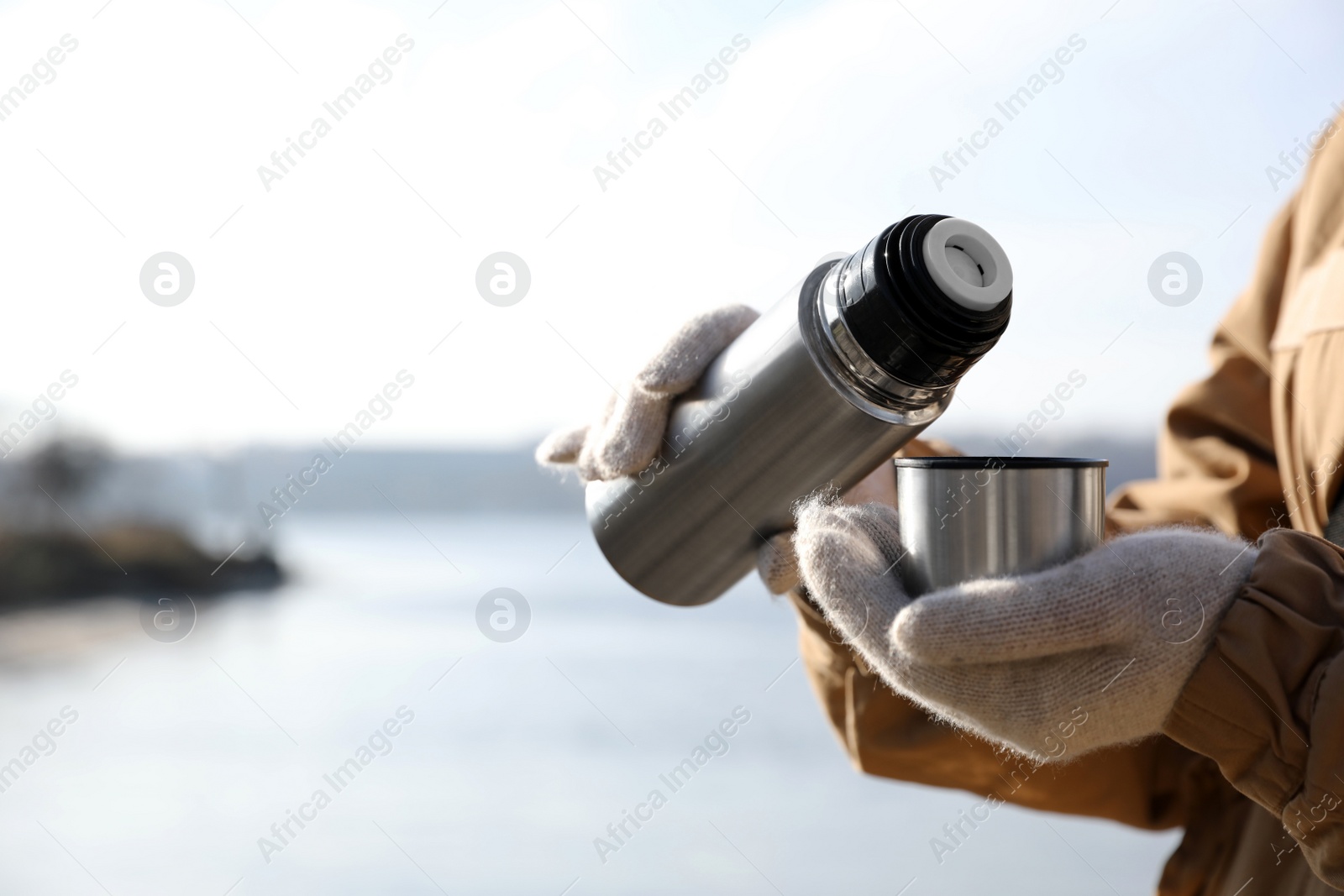 Photo of Woman pouring hot drink into cup from thermos outdoors, closeup