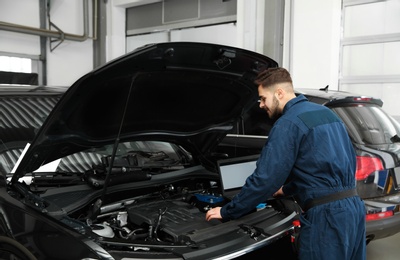 Photo of Technician checking car with laptop at automobile repair shop