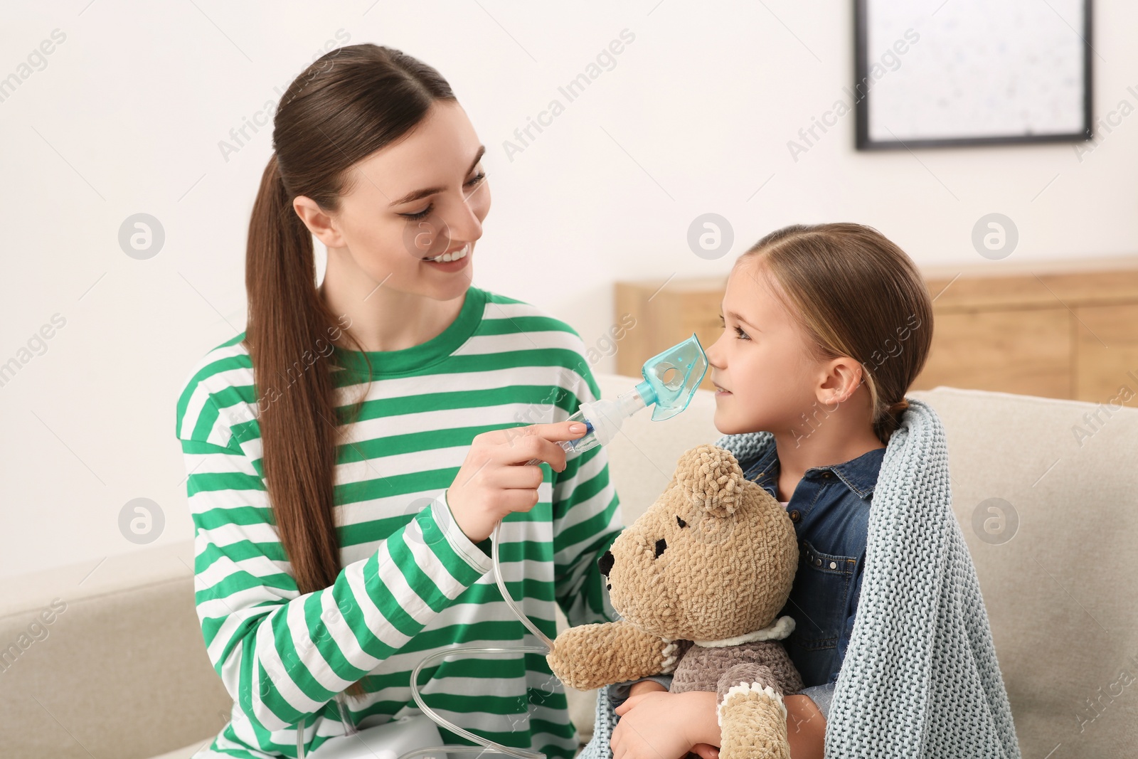 Photo of Mother helping her sick daughter with nebulizer inhalation at home