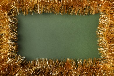 Photo of Frame of golden tinsel on olive background, top view. Space for text