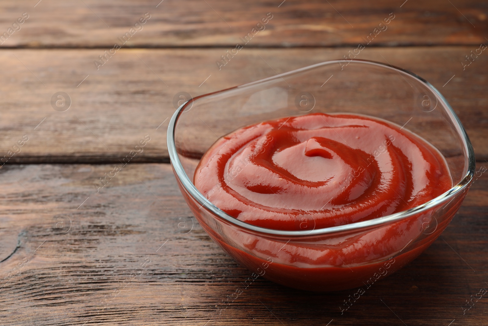 Photo of Bowl of tasty ketchup on wooden table, closeup. Space for text