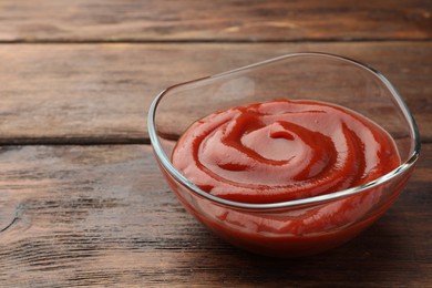Bowl of tasty ketchup on wooden table, closeup. Space for text