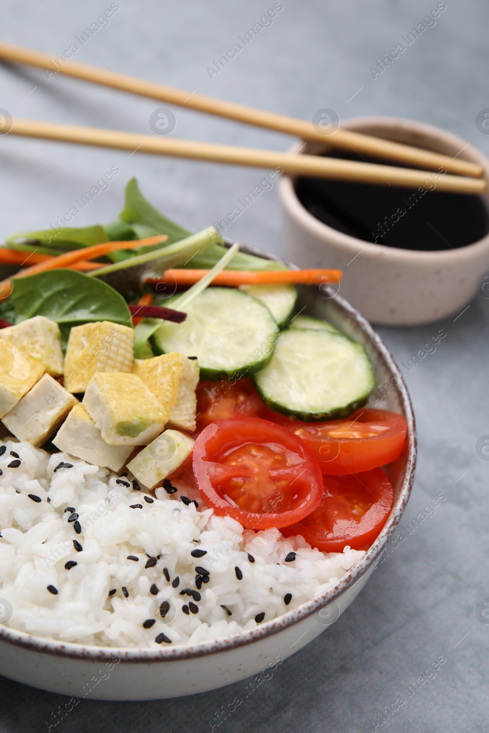 Photo of Delicious poke bowl with vegetables, tofu and mesclun served on light grey table