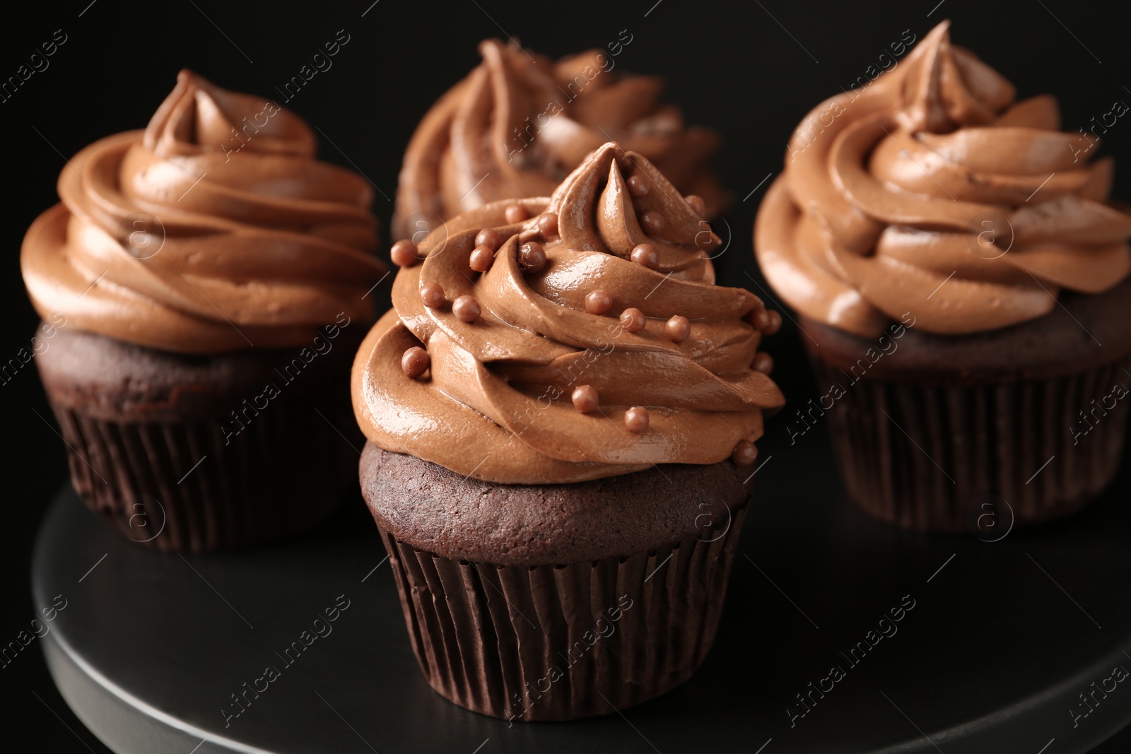 Photo of Delicious chocolate cupcakes with cream and beads on black table, closeup