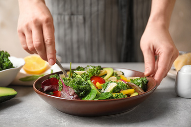 Photo of Woman cooking tasty kale salad on light grey table, closeup