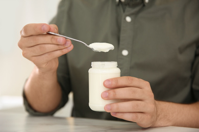 Young man with tasty yogurt at table, closeup