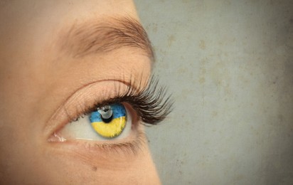 Image of Young woman on light grey background, closeup view of eye with Ukrainian flag reflection