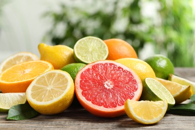 Photo of Different fresh citrus fruits and leaves on wooden table against blurred background, closeup