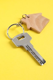 Photo of Key with keychain in shape of house on yellow background, closeup