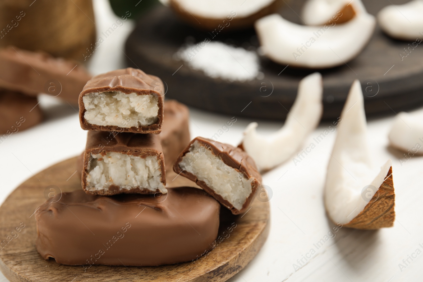 Photo of Delicious milk chocolate candy bars with coconut filling on white wooden table, closeup