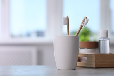 Photo of Bamboo toothbrushes in holder and cosmetic products on light grey table. Space for text
