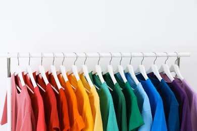 Rack with bright clothes on white background. Rainbow colors