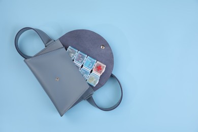Photo of Stylish women's bag with plastic pill box on light blue background, top view. Space for text